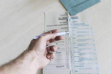 Mann hält Kugelschreiber über Wahlzettel auf Tisch - CHPF00854