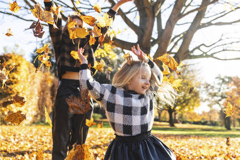 Mutter und Tochter spielen mit Herbstblättern im Park - WPEF05958
