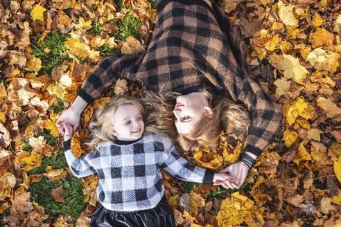 Mutter und Tochter liegen auf Herbstblättern im Park - WPEF05961