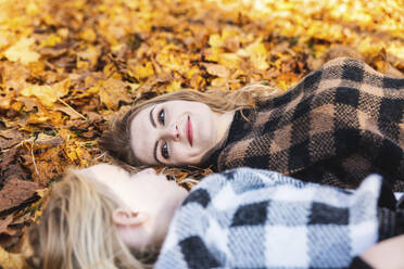 Smiling woman looking at daughter lying on autumn leaves in park - WPEF05962