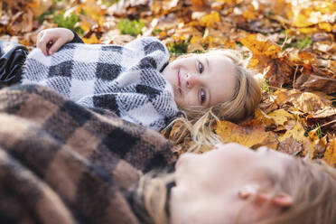 Lächelndes Mädchen sieht seine Mutter an, die auf Herbstblättern im Park liegt - WPEF05963