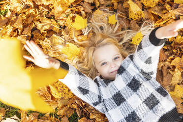 Verspieltes Mädchen liegt auf Herbstblättern im Park - WPEF05964