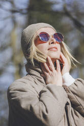 Blond woman wearing knit hat and sunglasses on sunny day - OMIF00780