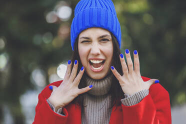 Young woman wearing blue knit hat gesturing with mouth open - OMIF00787