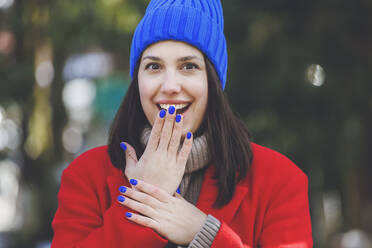 Surprise young woman with blue nail polish covering mouth with hand - OMIF00788