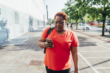 Woman using smart phone walking on footpath - MEUF05509