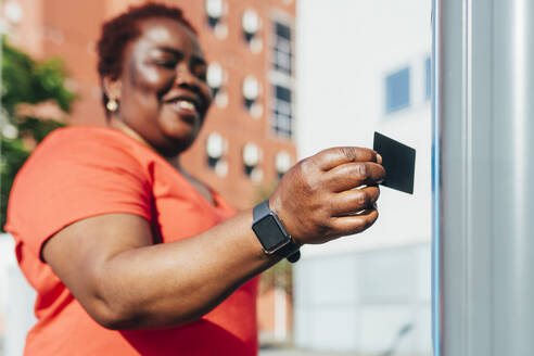 Lächelnde Frau beim Bezahlen mit Kreditkarte an einem sonnigen Tag - MEUF05563