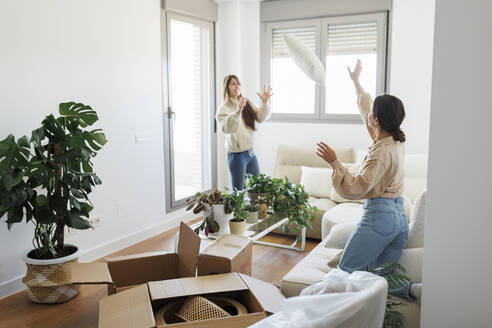 Frau wirft Kissen zu Freundin im Wohnzimmer zu Hause - MRRF02095