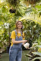 Happy woman watering plant in garden - SSGF00863