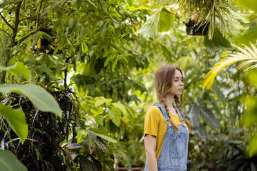 Thoughtful young woman with brown hair standing in garden - SSGF00865