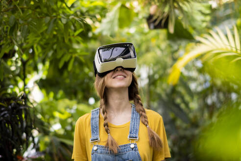 Lächelnde Frau mit Virtual-Reality-Simulator im Garten stehend - SSGF00870