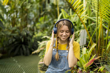 Glückliche Frau, die im Garten sitzend Musik über drahtlose Kopfhörer genießt - SSGF00871