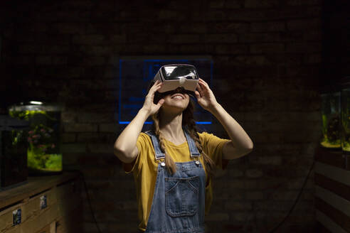 Smiling woman wearing virtual reality simulator in darkroom - SSGF00891