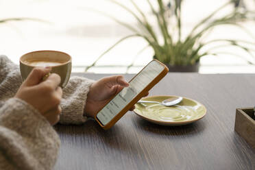 Hände einer Frau, die eine Kaffeetasse hält und ein Mobiltelefon in einem Café benutzt - SSGF00901