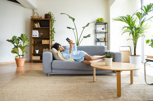 Glückliche junge Frau, die ein Mobiltelefon benutzt und zu Hause auf dem Sofa liegt - OIPF01706