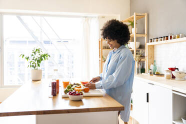 Happy woman cutting fruit on cutting board in kitchen at home - OIPF01709