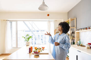 Schöne Frau, die eine Tomate fängt, stehend an der Kücheninsel zu Hause - OIPF01710