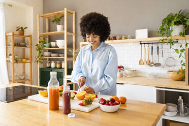 Lächelnde Frau schneidet Obst auf einem Brett in der Küche zu Hause - OIPF01715