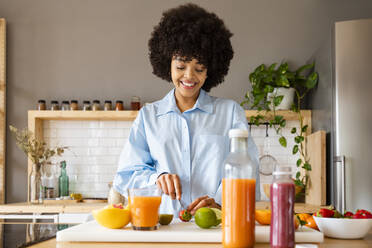 Beautiful woman cutting fruit with knife on board in kitchen at home - OIPF01720