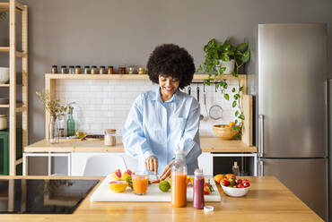 Young woman cutting fruit with knife on board in kitchen at home - OIPF01722