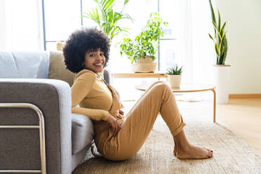 Lächelnde Afro-Frau lehnt zu Hause auf dem Sofa - OIPF01733