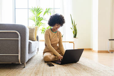 Glückliche Frau mit Laptop auf Teppich sitzend zu Hause - OIPF01736