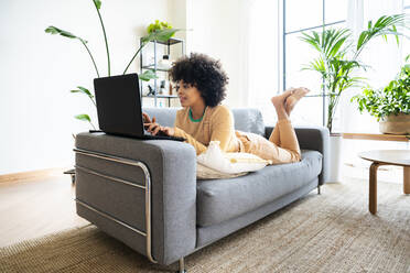 Junge Frau mit Laptop auf dem Sofa zu Hause liegend - OIPF01741