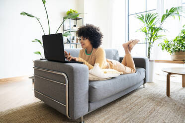 Young woman using laptop lying on sofa at home - OIPF01741