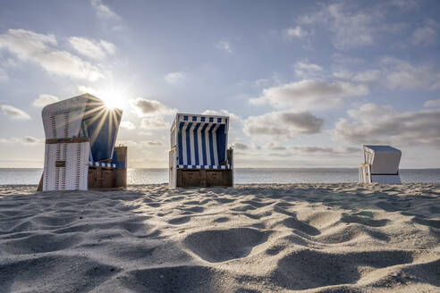 Deutschland, Schleswig-Holstein, Hornum, Morgensonne über leeren Strandkörben mit Kapuze am Sandstrand - KEBF02272