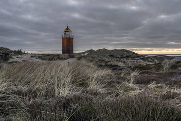 Deutschland, Schleswig-Holstein, Kampen, Grasbewachsener Strand in bewölkter Abenddämmerung mit Leuchtturm Rotes Kliff im Hintergrund - KEBF02274