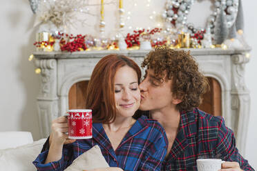 Man kissing girlfriend in front of fireplace at home - EIF04097