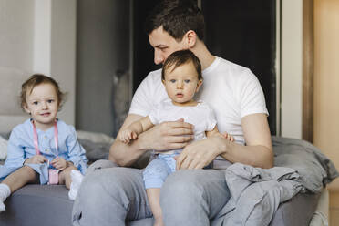 Mann mit Sohn und Tochter sitzt zu Hause auf dem Bett - SEAF00861