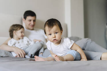 Niedlicher kleiner Junge mit Vater und Schwester im Hintergrund auf dem Bett zu Hause - SEAF00865