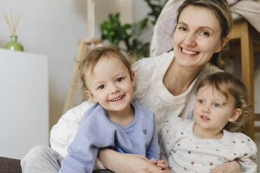Glückliche Mutter mit Zwillingstöchtern im Wohnzimmer sitzend - SEAF00882