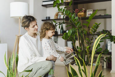 Girl watering potted plant with mother in living room - SEAF00888