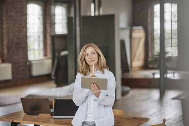 Nachdenkliche Geschäftsfrau mit Tablet-PC, der auf einem Tisch zu Hause steht - FMKF07564