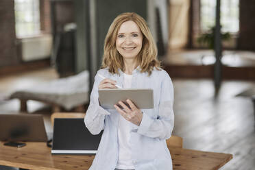 Smiling businesswoman with tablet PC leaning on table at home - FMKF07566