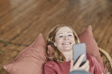 Glückliche Frau, die ein Smartphone benutzt und zu Hause auf dem Sofa liegt - FMKF07568