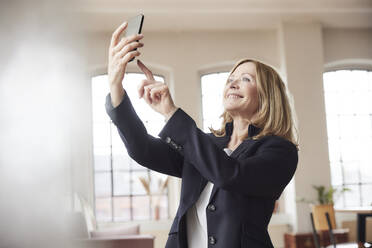 Glückliche Geschäftsfrau nimmt Selfie durch Smartphone zu Hause - FMKF07586