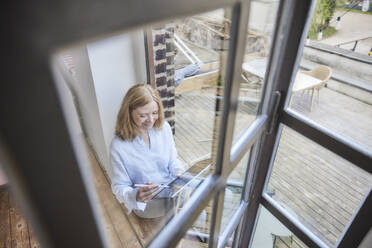 Geschäftsfrau mit Tablet-PC an der Tür sitzend - FMKF07614