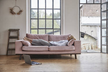 Frau entspannt auf Sofa im Wohnzimmer zu Hause - FMKF07624