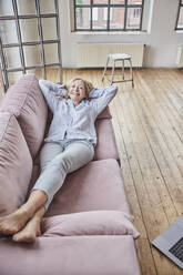 Glückliche Frau mit Händen hinter dem Kopf auf dem Sofa zu Hause liegend - FMKF07625