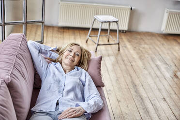 Smiling woman lying on sofa at home - FMKF07627