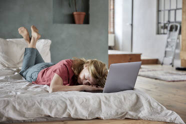 Müde Frau liegt mit Laptop auf dem Bett zu Hause - FMKF07641