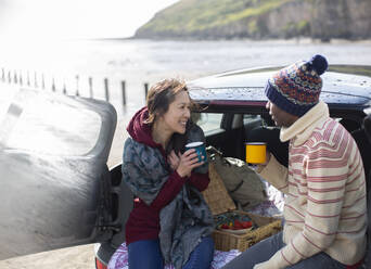Glückliches Paar trinkt Kaffee auf dem Rücksitz eines Autos am Strand - CAIF32339