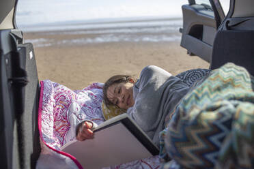 Gelassene Frau mit Skizzenbuch auf dem Rücksitz eines Autos am Strand - CAIF32344