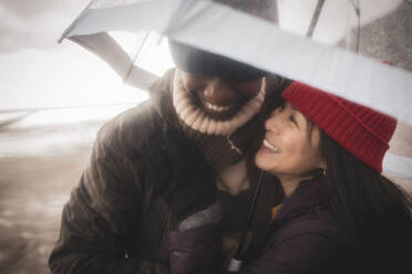 Glückliches Paar unter Schirm am nassen Winterstrand - CAIF32349