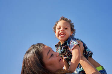 Porträt einer Mutter, die ihren glücklichen, sorglosen Sohn mit Down-Syndrom hochhebt - CAIF32356