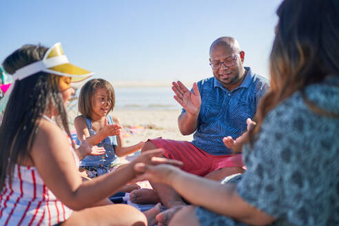 Familie spielt Klatschspiel am sonnigen Strand - CAIF32360