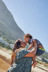 Happy, affectionate mother kissing son on sunny beach - CAIF32361
